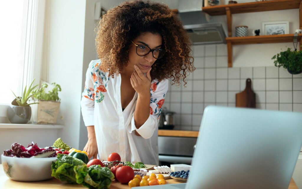 Busy professional in the kitchen looking at a laptop while preparing healthy food for a 5-day fat loss plan.